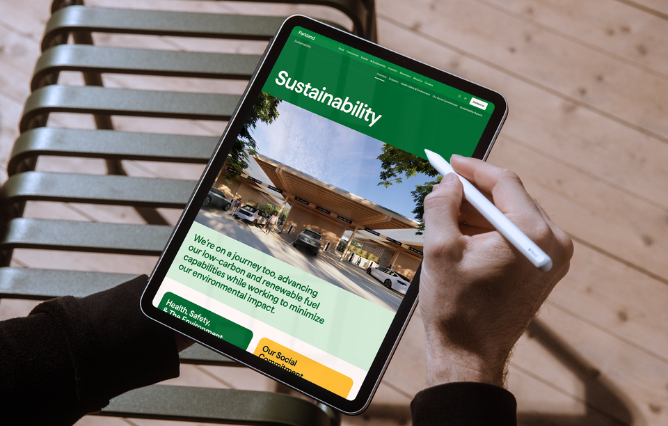 A person holding a tablet showing the Parkland website. It shows the Parkland Sustainability page, with an image of an electric vehicle charging station, the headline Sustainability, and the subhead We're on a journey too, advancing our low-carbon and renewable fuel capabilities while working to minimize our environmental impact.