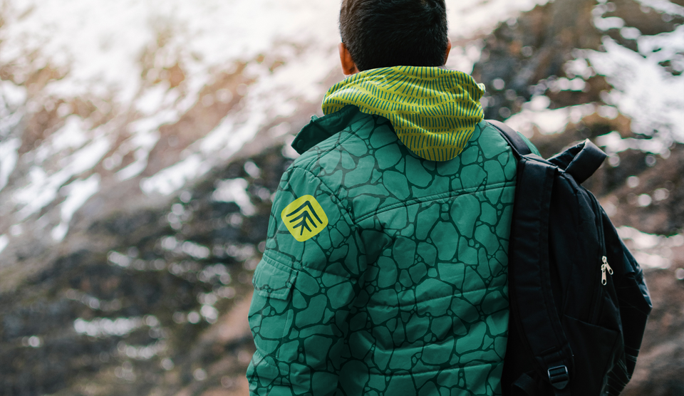 a main wearing a heavy winter jacket in green, with a pattern of Rainforest to Rockies printed on it and the arrow icon on his shoulder