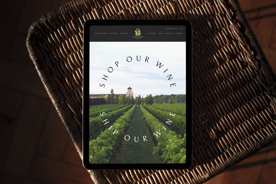 an iPad displaying the Two Sisters Vineyards website, an image of a vineyard with the headline Shop Our Wine, Ship Our Wine