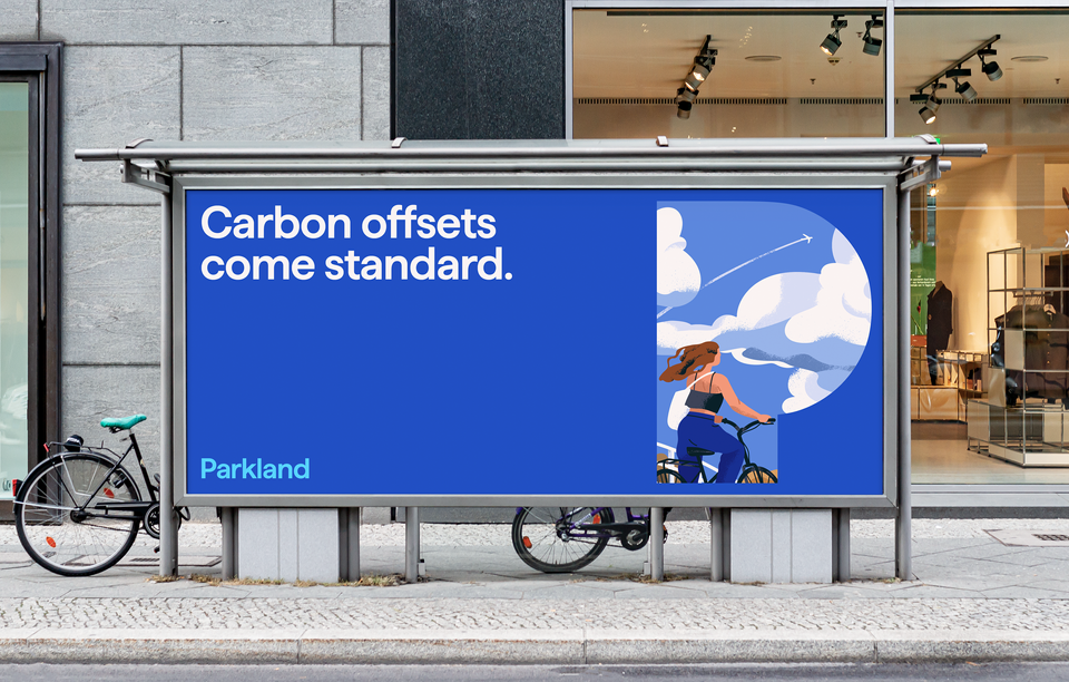 A transit shelter billboard with the text Carbon offsets come standard. An illustration of a woman on a bicycle looking up at an airplane in the sky is shown within the Parkland P logo