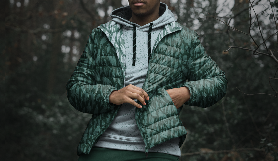 a man wearing a puffer jacket in blues and greens, with a pattern of The Great Wilderness printed on it