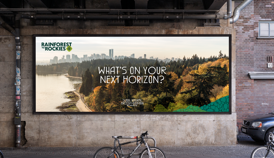 a billboard under a railway overpass advertising Rainforest to Rockies, with a photo of Stanley Park and the Vancouver skyline and the headline What’s On Your Next Horizon?